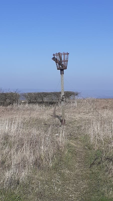 A metal beacon structure atop a grassy hill, surrounded by sparse vegetation and a clear blue sky.