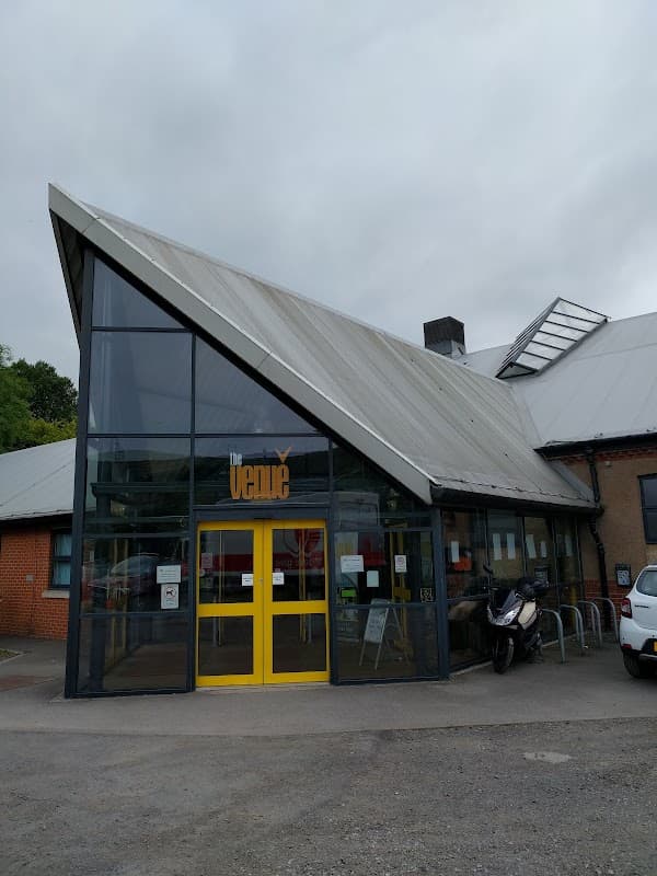 Modern building with a slanted roof, large glass entrance, yellow doors, and signage reading "The Venue."