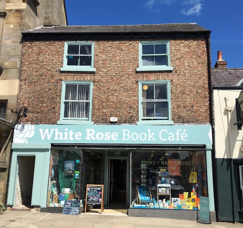 Charming brick building with a teal sign for White Rose Book Café, featuring books displayed in the window and a clear blue sky.
