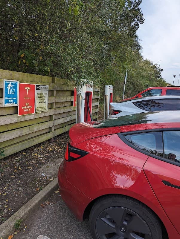 Tesla Supercharger station in Tingley, Yorkshire, with charging points and a red Tesla parked nearby.