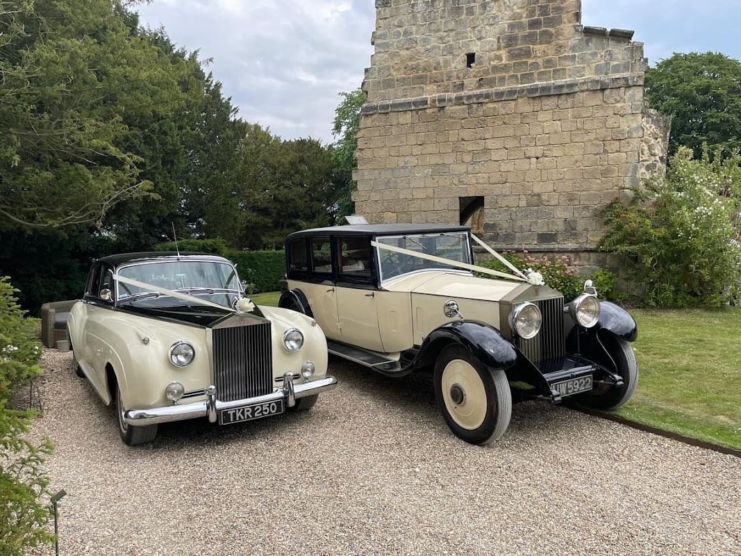 Two classic wedding cars parked near a stone building, surrounded by greenery in Tockwith, Yorkshire.