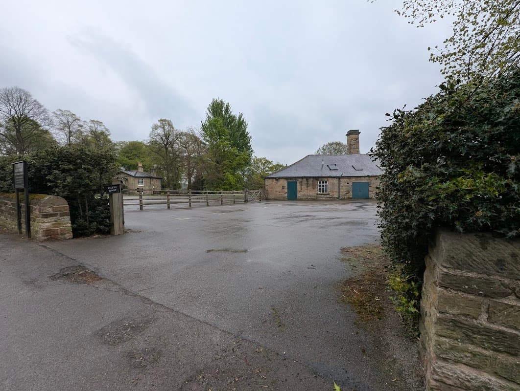 Pay & Display car park with a stone building, trees, and a gravel path in Wentworth, Yorkshire.