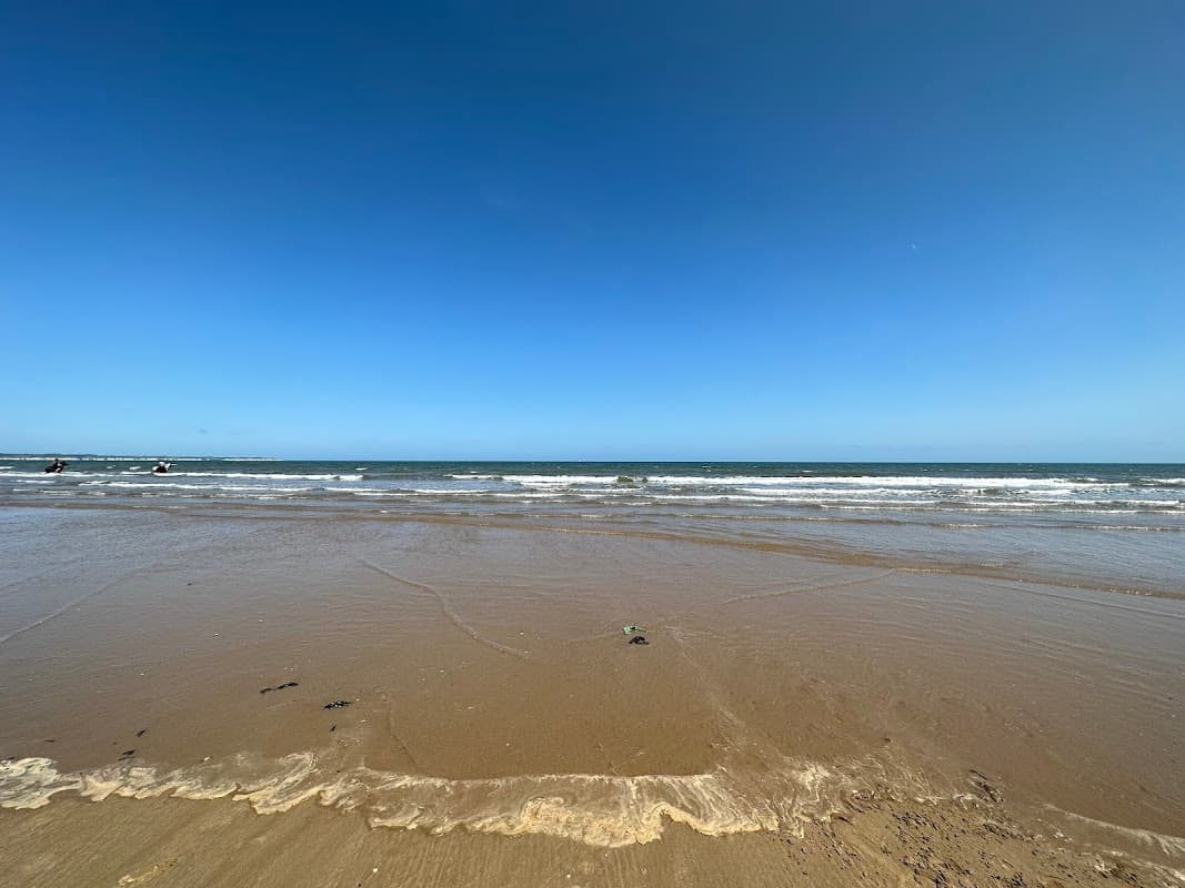 Sandy beach with gentle waves under a clear blue sky at East Yorkshire Coast AONB, Wilsthorpe.