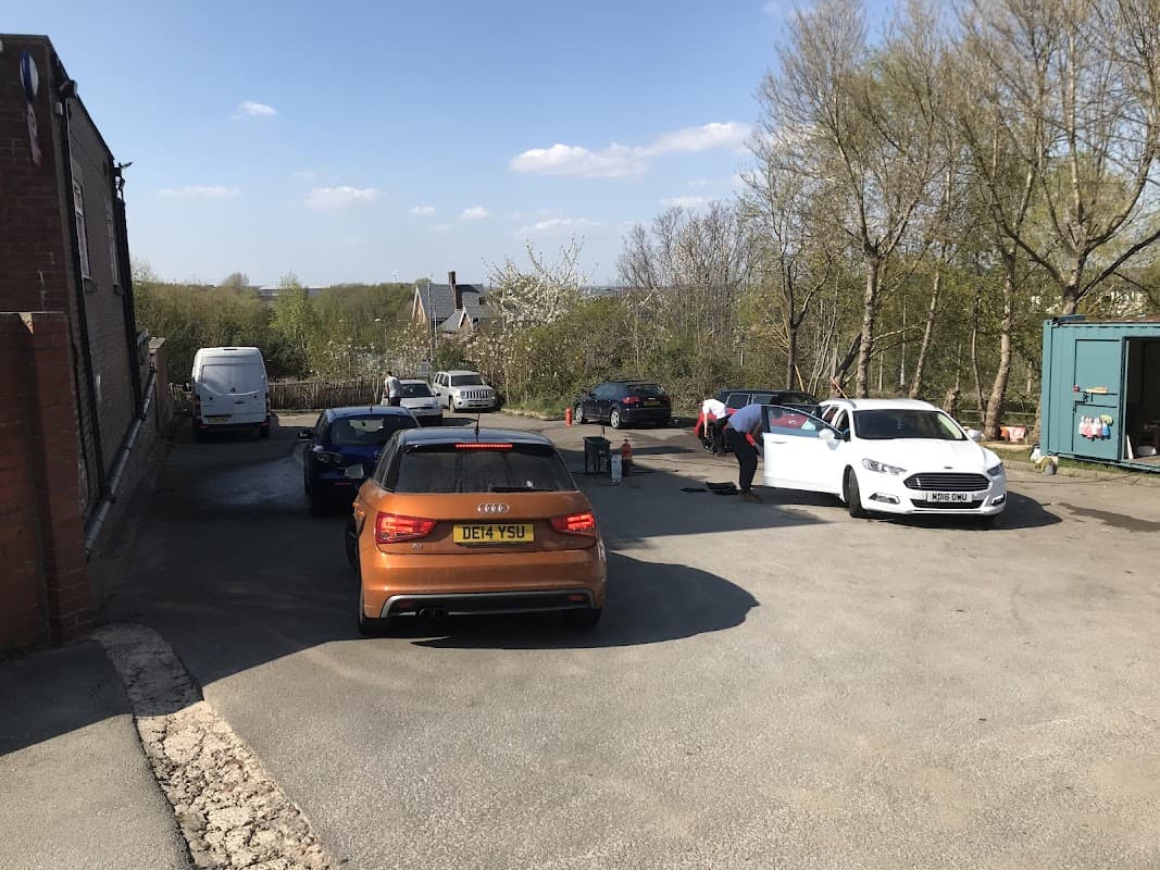 Woodhouse Hand Car Wash with several cars parked and staff washing vehicles under a clear blue sky.
