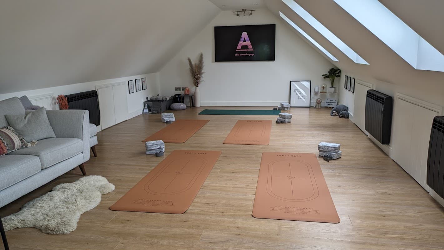 Yoga studio with mats arranged on wooden floor, cozy seating area, and a screen displaying "Abbi Santosha Yoga."
