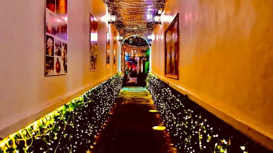 Twinkling fairy lights line a narrow corridor, leading to a cozy, warmly lit restaurant.