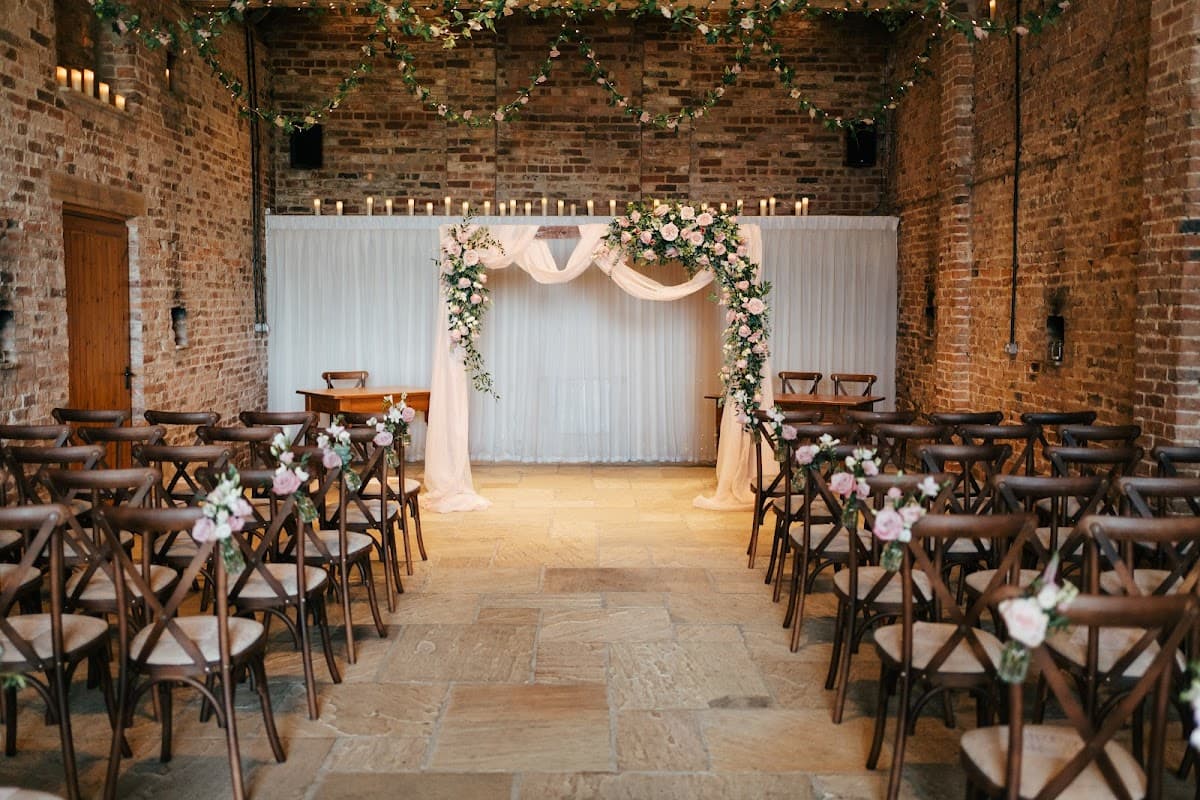 Floral-decorated wedding venue with wooden chairs, a floral arch, and soft drapery against a rustic brick backdrop.