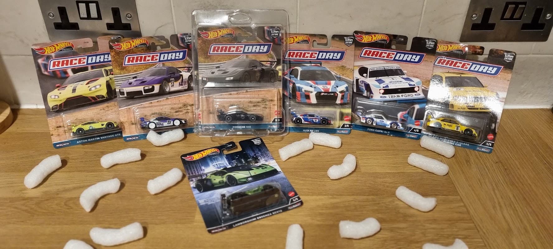 Hot Wheels cars in packaging displayed on a wooden surface, surrounded by packing peanuts.