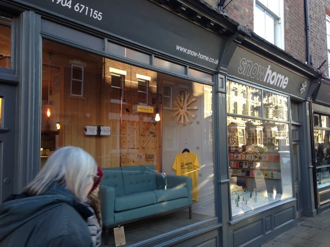 Charming gift shop exterior featuring a large window display with a blue sofa, merchandise, and a yellow shirt.