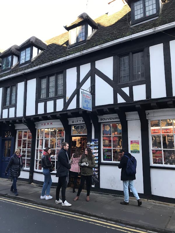 Charming gift shop with Tudor-style architecture, people browsing outside, and colorful souvenirs displayed in windows.
