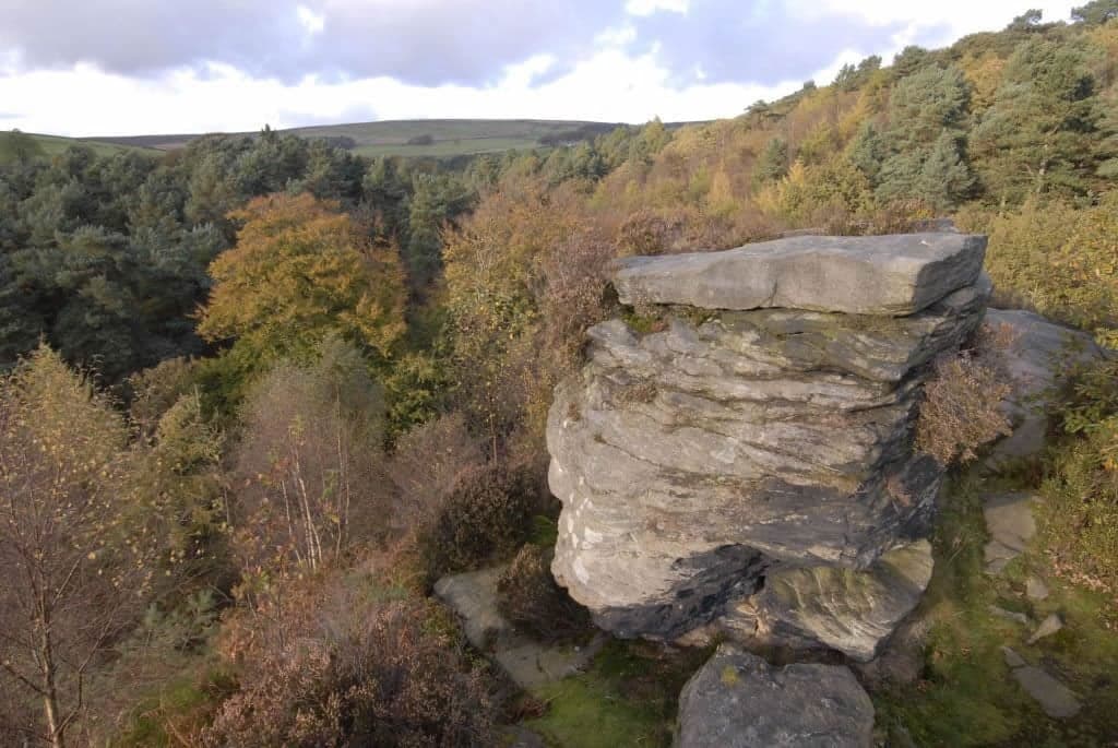 Rocky outcrop surrounded by autumnal trees in Hardcastle Crags, Yorkshire, under a cloudy sky.