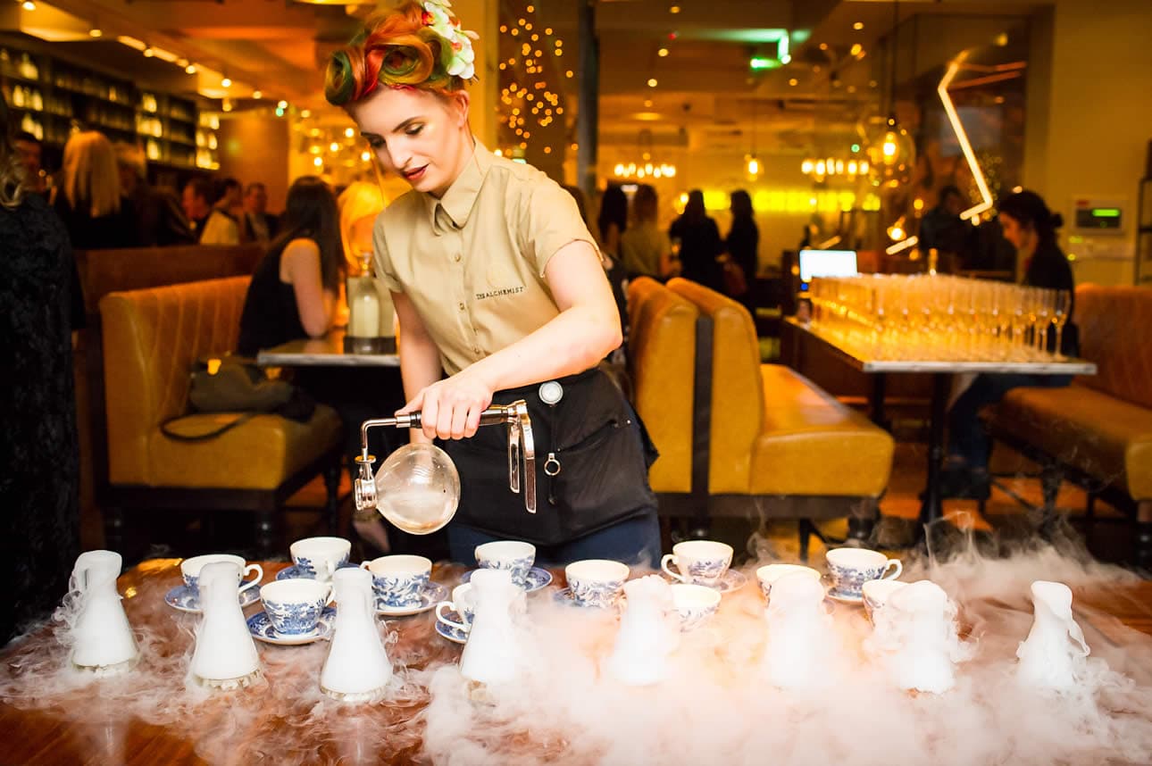 Bartender at The Alchemist, Greek Street, Leeds, pours drinks with dramatic smoke effects in a stylish, bustling venue.