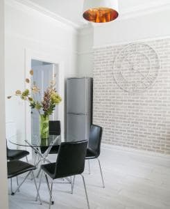Modern dining area in Glebe Apartment 1, Harrogate, featuring a glass table, black chairs, and a brick accent wall.