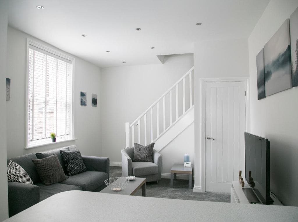 Modern living room in 71 East Parade, Harrogate; grey sofas, white walls, staircase, large window with blinds.