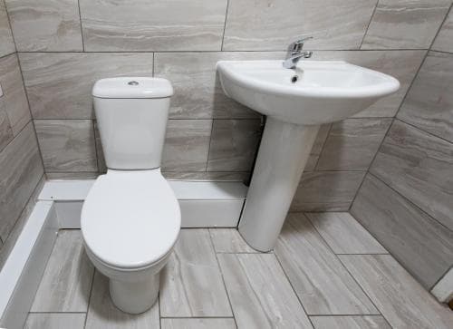 Modern bathroom in High Bank Hotel, Leeds, featuring tiled walls, a white toilet, and a pedestal sink.