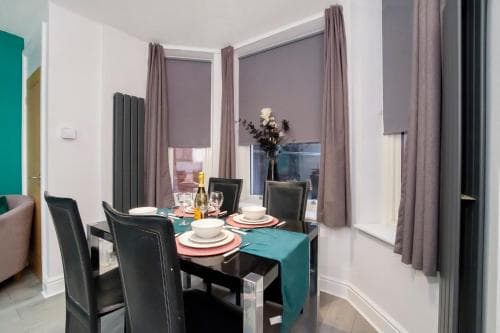 Dining area with set table, teal runner, black chairs, large windows with grey curtains, and vase with flowers in York.