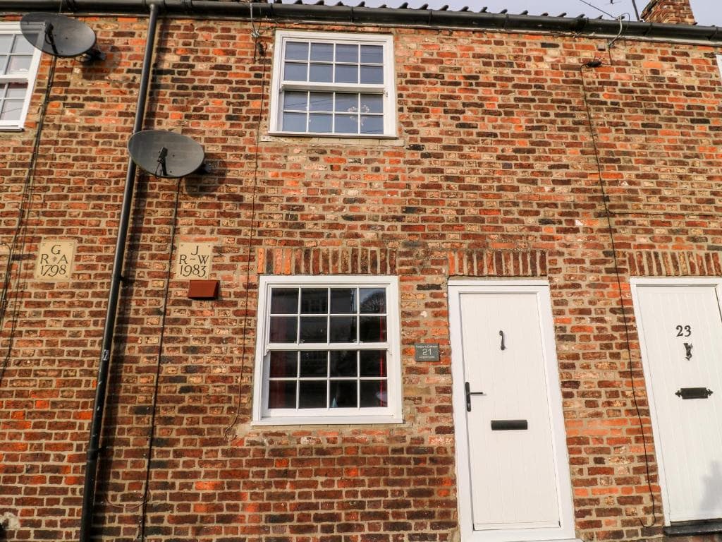 Charming brick cottage with white doors and windows, nestled in Yorkshire's Nafferton, featuring historical plaques.