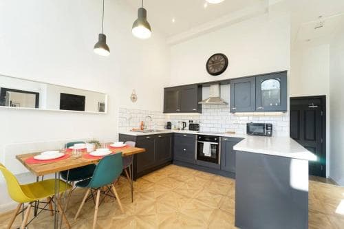 Bright Leeds apartment kitchen with dark cabinets, dining table, colorful chairs, and modern lighting.