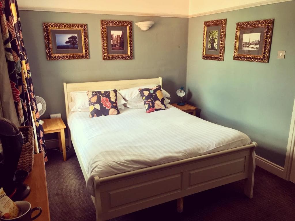 Cozy bedroom at The Royal Oak Ripon, featuring a double bed, floral curtains, and framed art on pastel green walls.