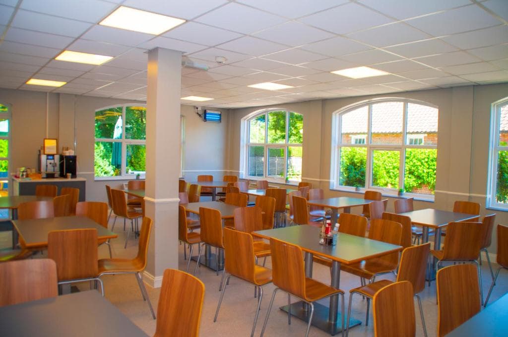 Bright dining area at Stableside, York, with wooden chairs, large windows, and green views.