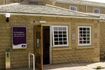 Elegant hotel room with a plush bed, gray bedding, side table with flowers, and modern pendant lights.