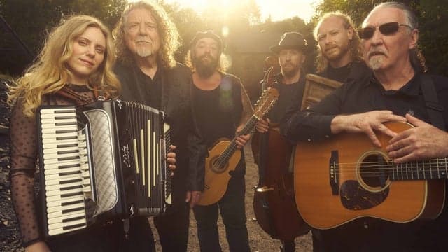 Musicians with guitars and accordion standing outdoors at sunset, surrounded by trees, creating a warm, rustic atmosphere.