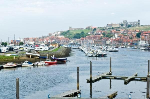 Harbor with sailboats, surrounded by colorful hillside buildings and a distant view of a historic abbey on the hilltop.