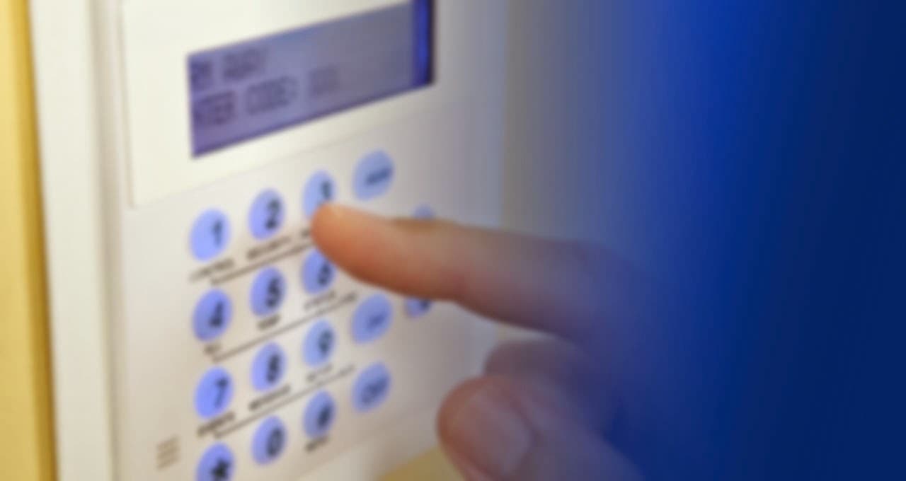 A hand pressing buttons on a security system keypad with a digital display.