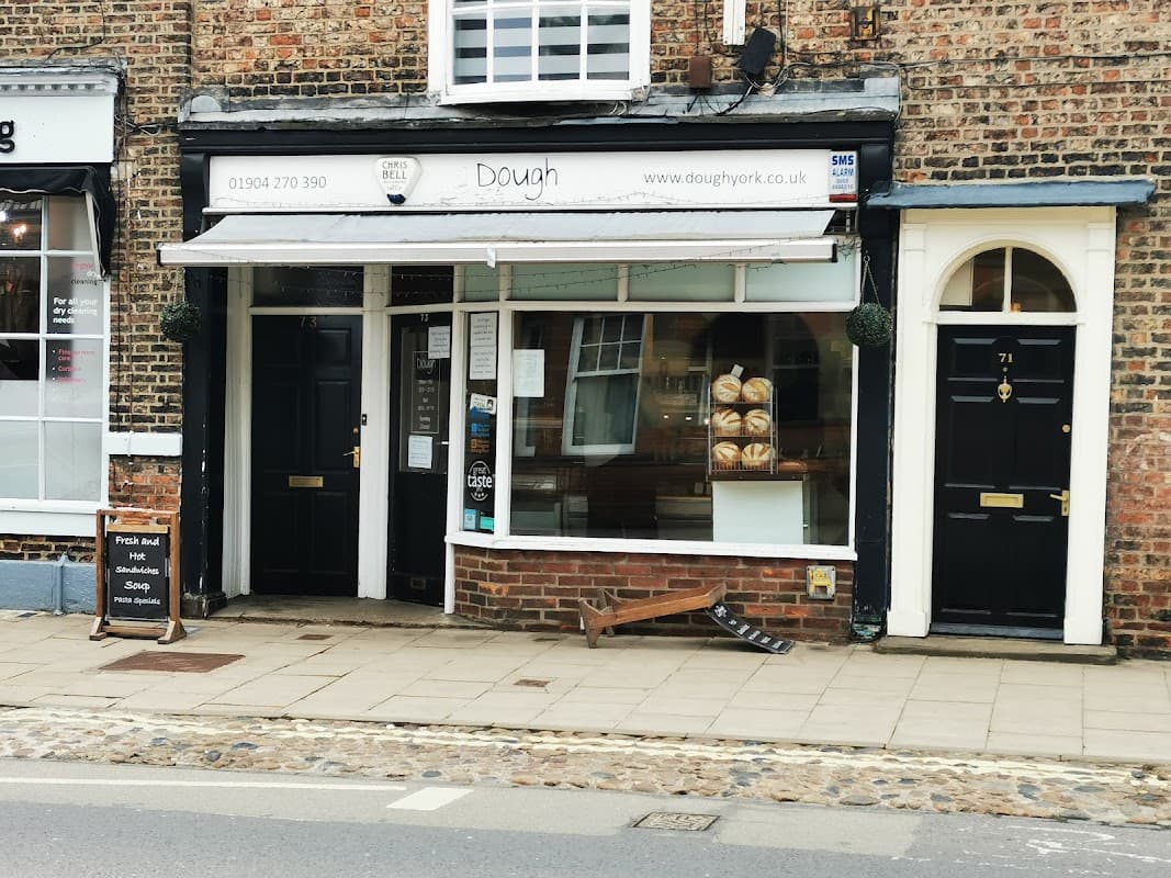 Quaint bakery "Dough" with large window displaying fresh bread, black doors, and cobblestone street in York, Yorkshire.