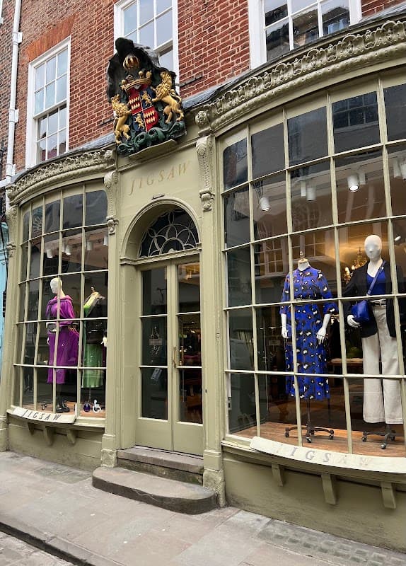 Storefront of Jigsaw in York, featuring large windows displaying colorful clothing and a decorative crest above the entrance.