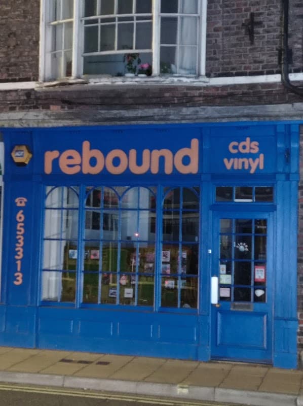 Bright blue storefront of "Rebound" music shop, featuring large windows and signage for CDs and vinyl.
