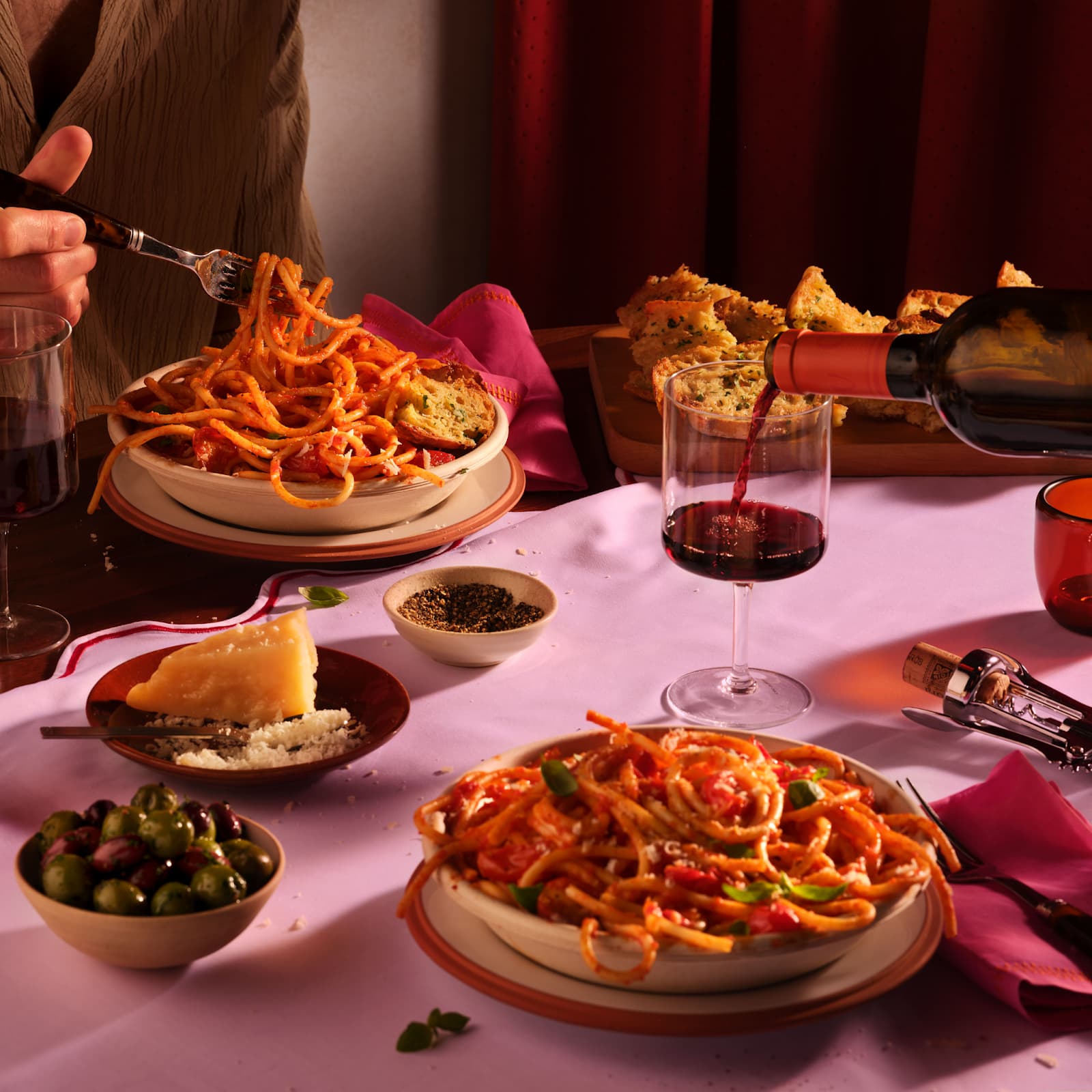 A romantic table setting featuring plates of pasta, wine, and olives, creating a cozy atmosphere for Valentine's Day.