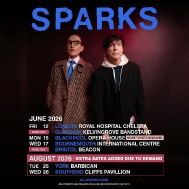 Two musicians in stylish outfits stand against a vibrant concert backdrop, promoting their return to York's Barbican.