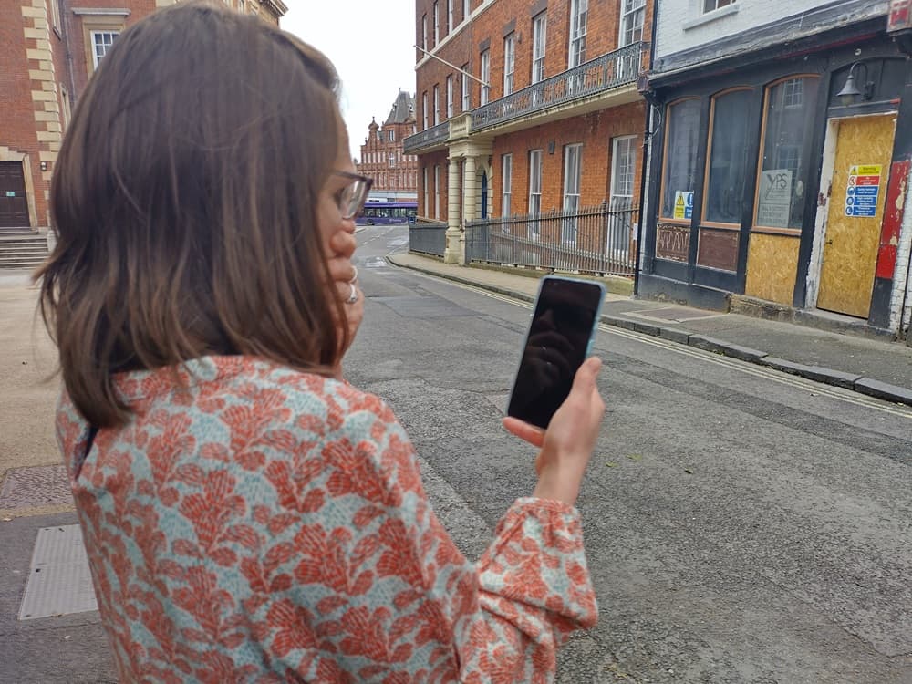 Woman in patterned shirt looking at smartphone on a city street