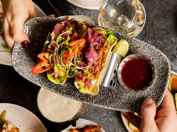 Hands serving gourmet tacos with pink toppings and sauce