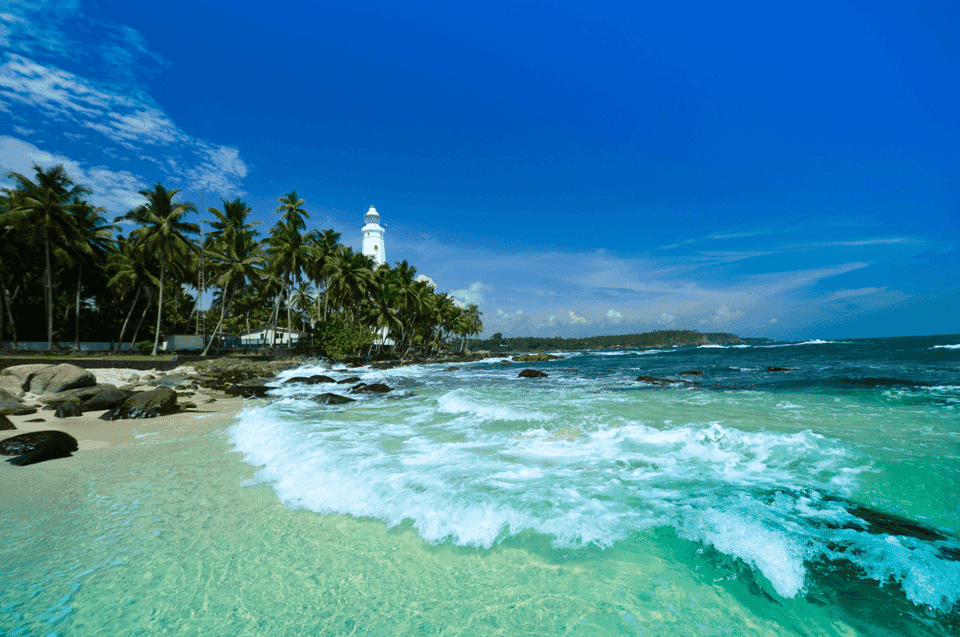 Lighthouse by palm-lined beach with clear blue sky
