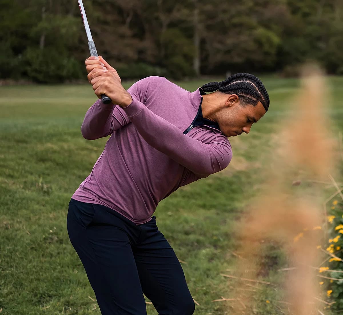 Person in purple sweater swinging golf club on lush course