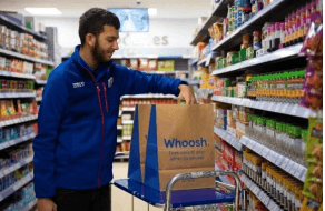 Store employee in uniform placing items in delivery bag