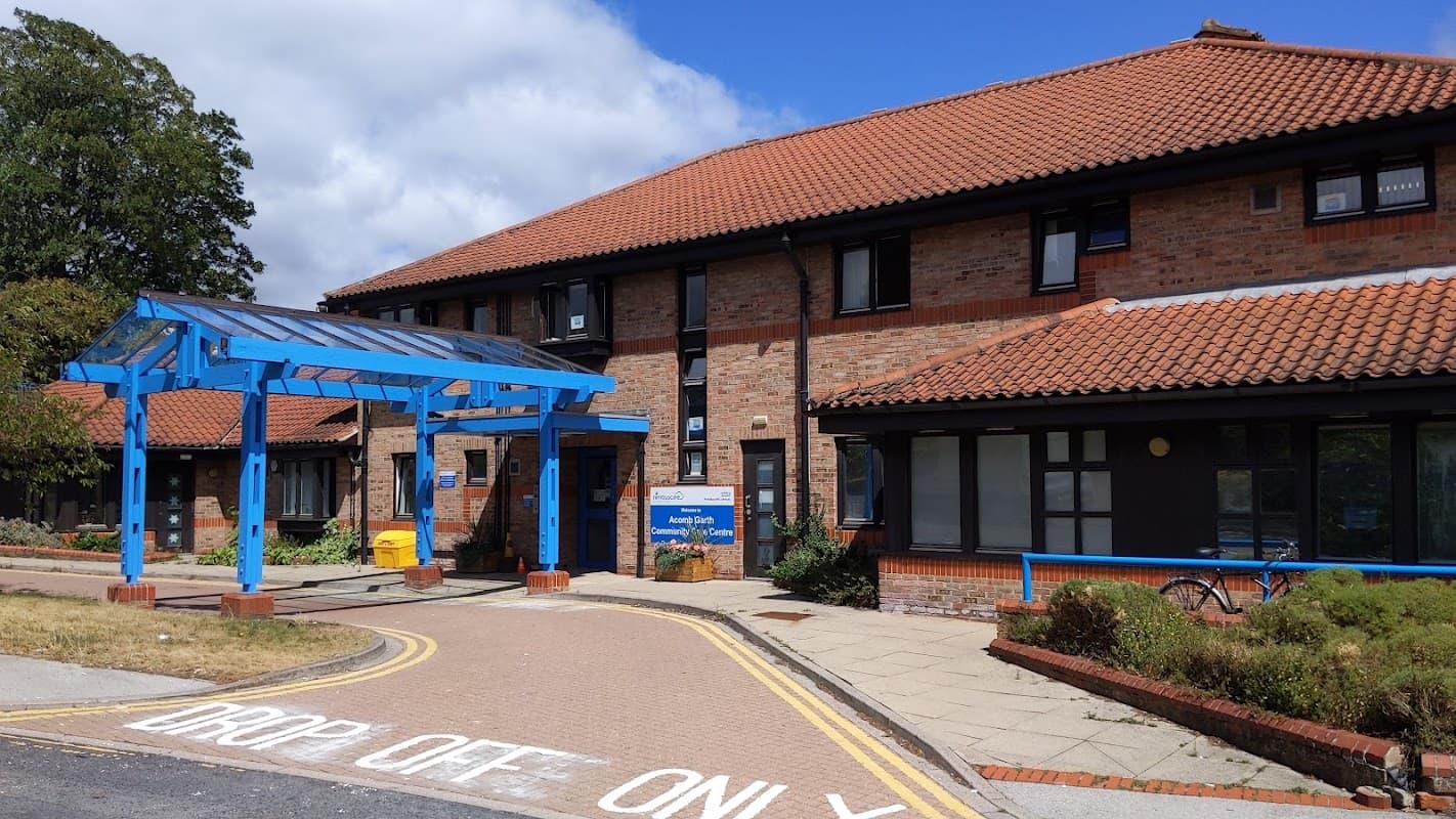 Blue canopy entrance to Nimbuscare Acomb Garth Community Care Centre, with brick buildings and a drop-off area.