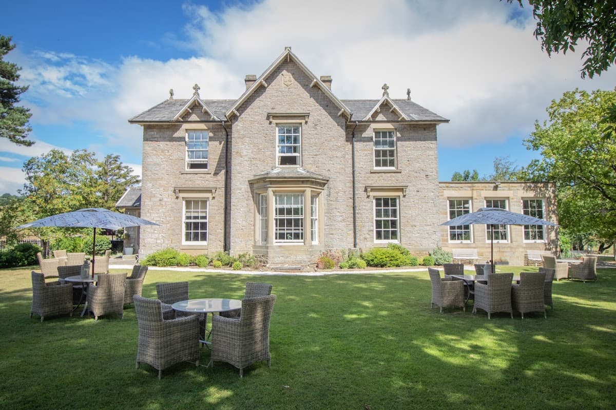 Elegant stone building surrounded by lush greenery, featuring outdoor seating with umbrellas in a picturesque setting.