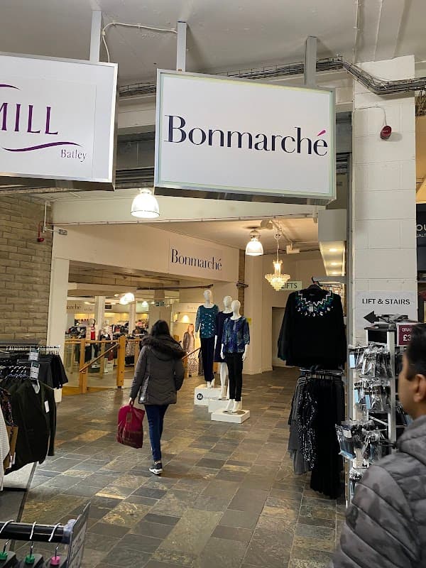 Entrance to BonmarchΓ© with clothing displays and shoppers in a well-lit retail space at Batley Mill.
