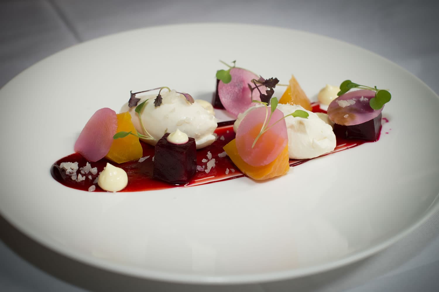 Elegant dish with colorful beetroot, dollops of cream, and microgreens on a white plate, arranged artistically.