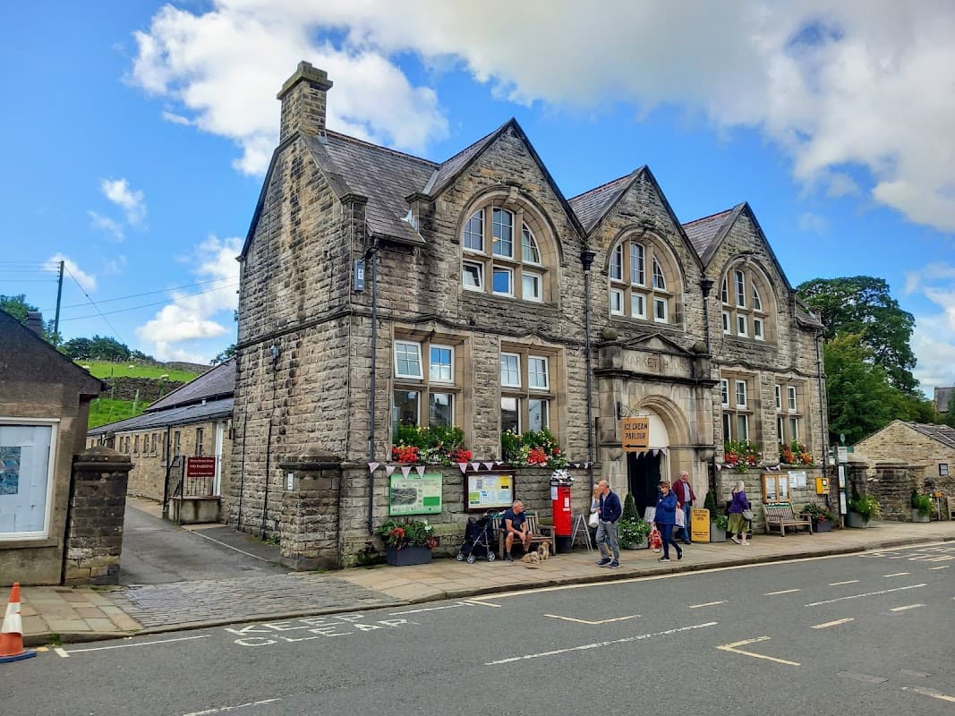 Historic stone building with arched windows, colorful flower boxes, and people entering, set against a blue sky.
