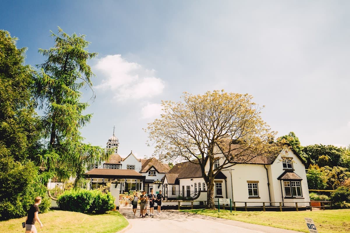 Bishop Burton College's charming venue features a large tree, lush greenery, and a historic building under a blue sky.