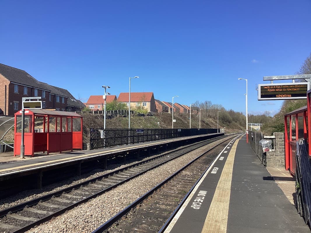 Railway station platform in Cottingley, Yorkshire, with red shelters, track, and residential buildings in the background.