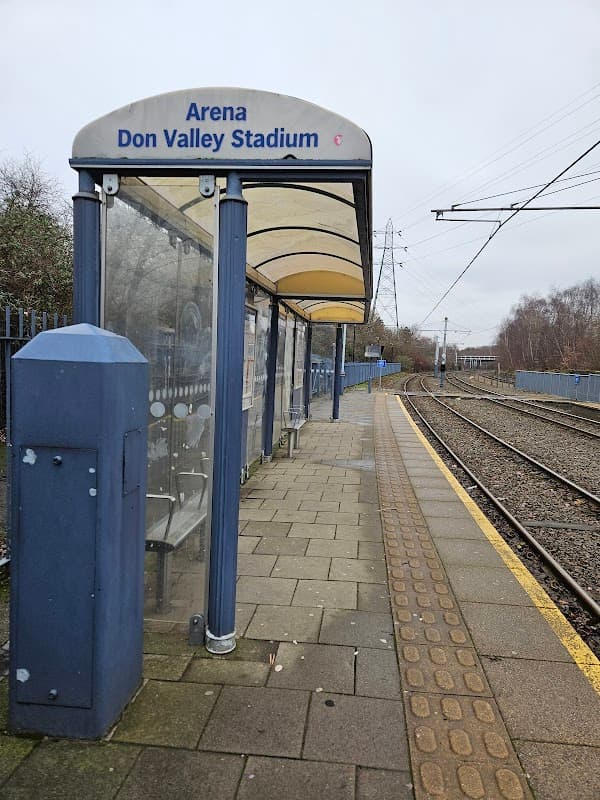 Shelter at a train station with "Arena Don Valley Stadium" sign, adjacent to railway tracks and paved platform.