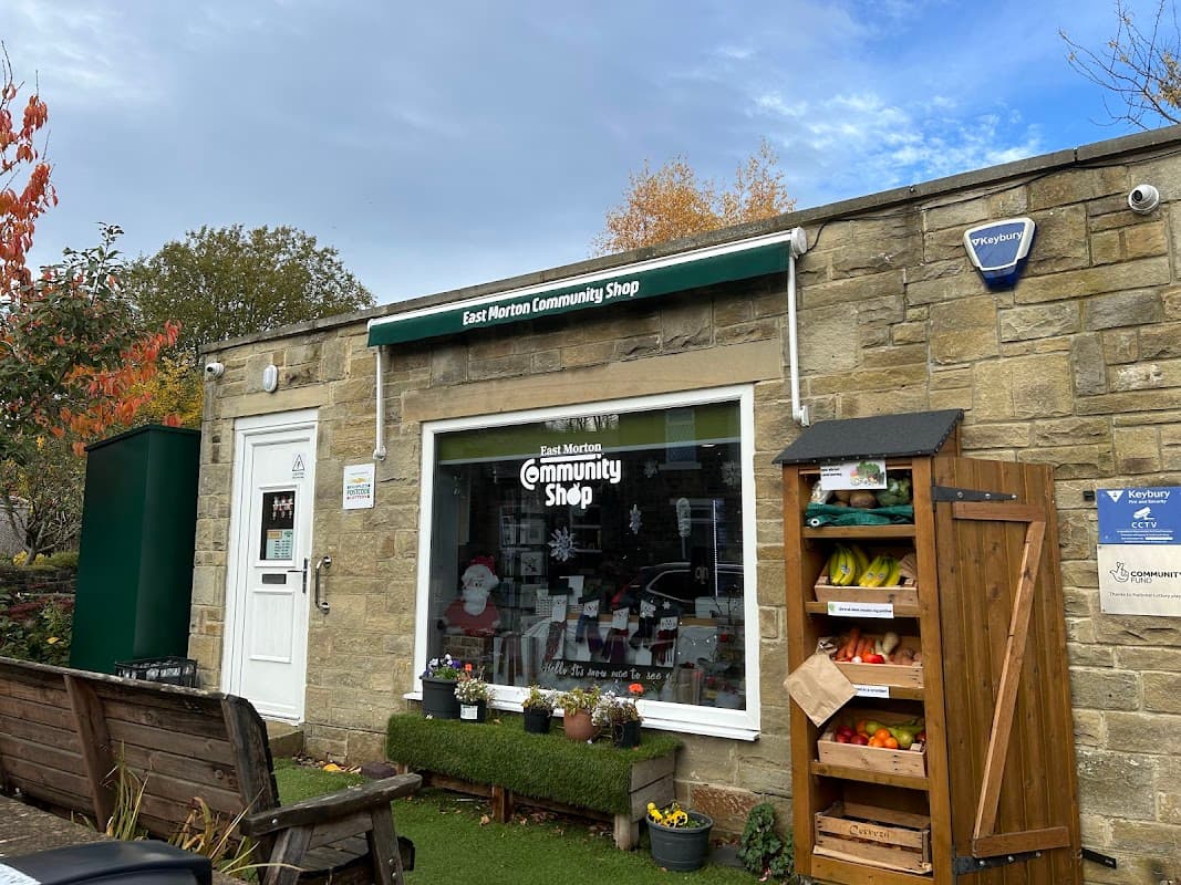 East Morton Community Shop with stone exterior, green awning, display of produce, and festive decorations in window.
