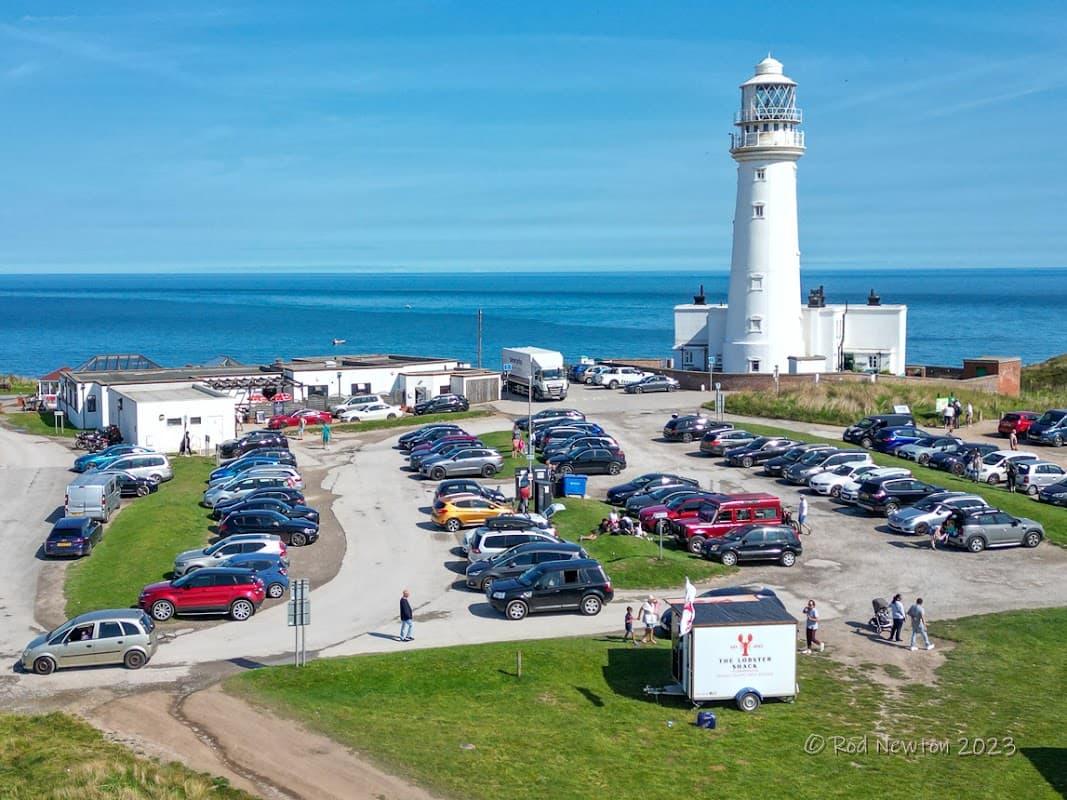 Lighthouse beside a busy car park with numerous vehicles and visitors, overlooking the sea at Flamborough Head.