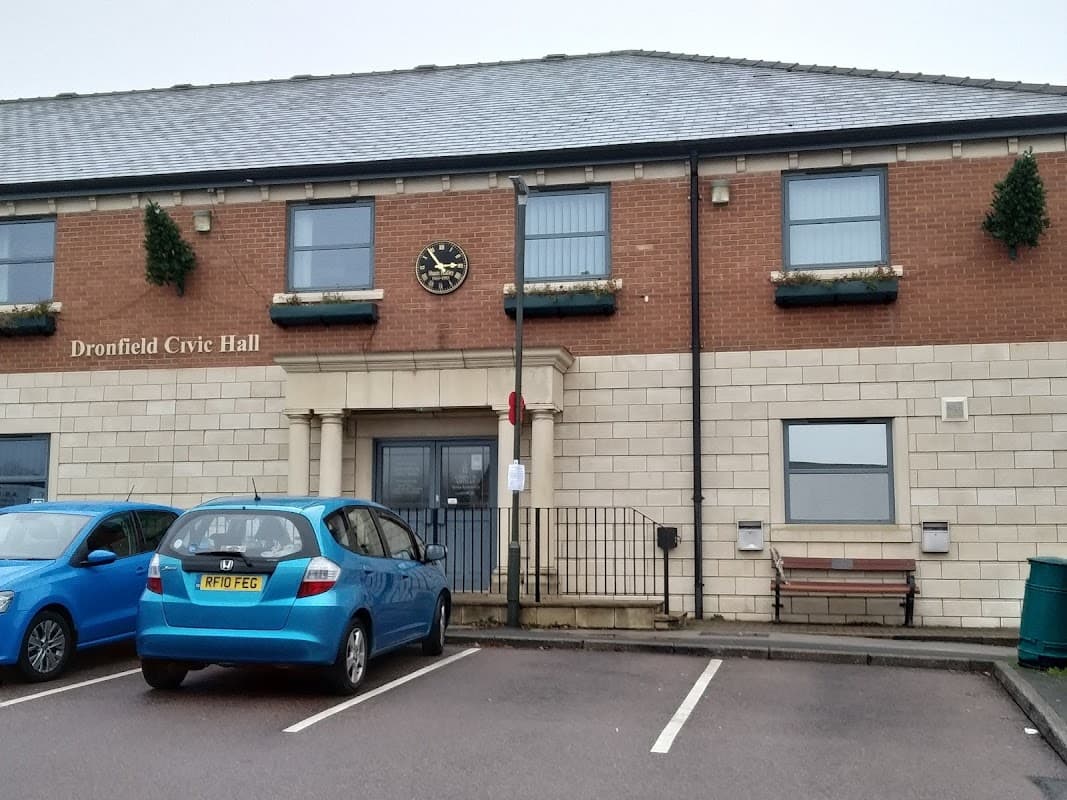 Dronfield Civic Hall with a clock, parking spaces, and a blue car in front. Greenhill, Yorkshire. Free parking sign visible.