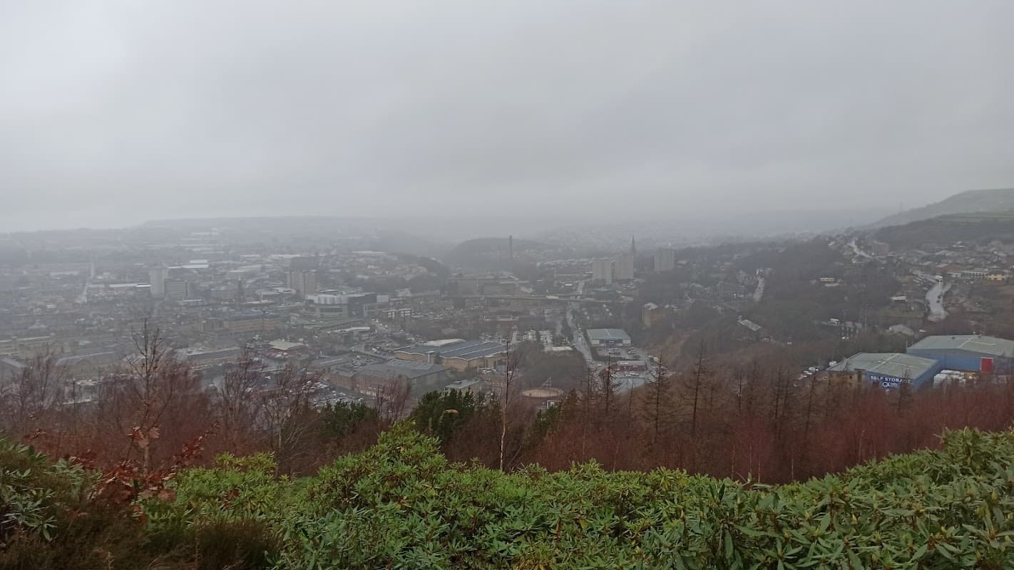 Foggy view of Halifax, Yorkshire, showcasing urban buildings and hills, with trees in the foreground.
